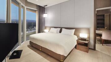 A modern hotel room with a large bed, bedside tables, a TV, and a city view.