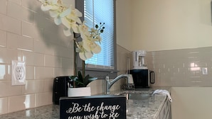 Eine Küche mit weißen Fliesen, einer schwarzen Arbeitsplatte, einer Kaffeemaschine und einem Schild mit einem motivierenden Spruch.