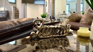 Ein modernes Wohnzimmer mit einer Ledersofa, einem Glastisch und einem dekorativen Metallschild.