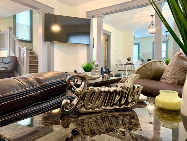 A modern living room with a leather sofa, a glass coffee table, and a decorative metal sign.