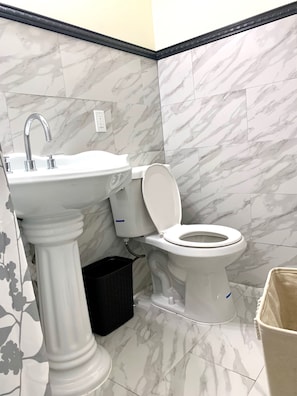 A bathroom with a pedestal sink, a toilet, and marble-patterned walls.
