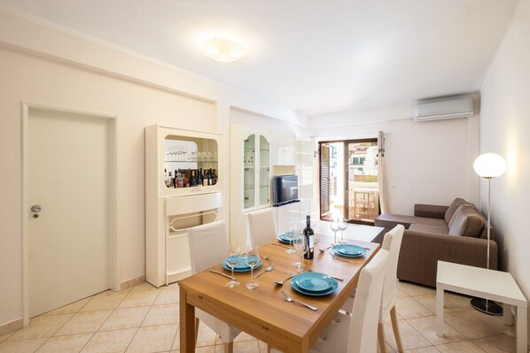 A dining area with a wooden table set for four, a sofa, and a TV in the background.