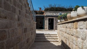 Un étroit couloir en pierre, avec des marches menant à une porte, flanqué de murs en pierre et d’une rambarde en métal.