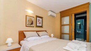Un lit bien fait, avec du linge de lit blanc, une lampe de chevet et un climatiseur fixé au mur.