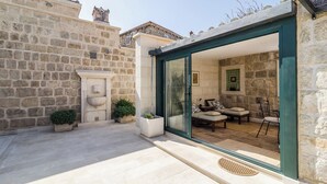 Un bâtiment en pierre doté d’une porte en verre qui donne sur un patio aménagé avec des sièges et une cheminée en pierre.
