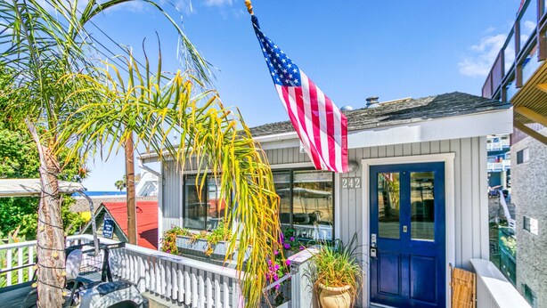 Um imóvel residencial com porta azul, varanda com corrimão e uma bandeira americana.