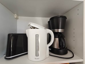 A white mug with a measurement scale, a black coffee maker, and a black electronic device on a shelf.