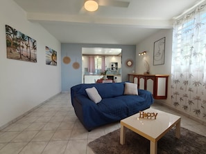 A living room with a blue sofa, a coffee table, and a kitchen in the background.