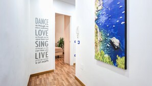 A hallway with a motivational quote on the wall, a wooden floor, and a large painting of a coastal scene. - Loving Times Apartment (Sorrento)