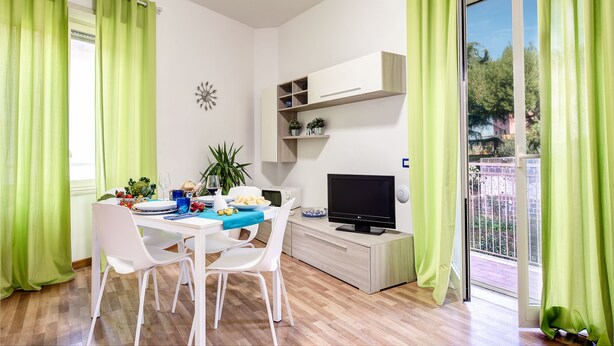 A modern living room with a dining area, a flat-screen TV, and a balcony with green curtains. - Loving Times Apartment (Sorrento)
