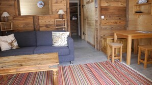 Una habitación acogedora con detalles de madera, un sofá con un cojín de ciervo, una mesita pequeña y una alfombra estampada.