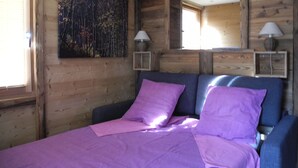 Un dormitorio de cabaña de madera con una cama, ropa de cama morada y dos lámparas de noche.