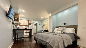 Une chambre d’hôtel de taille réduite, comprenant un lit, une petite kitchenette, une télévision et une carte affichée au mur.