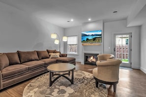 A living room with a sofa, armchair, coffee table, fireplace, TV, and a view of the outdoors. - Spacious Townhome with Fireplace (Ellicottville)