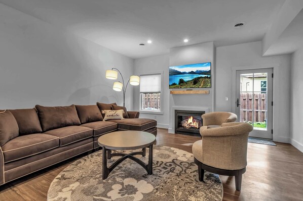 Una sala de estar con sofá, sillón, mesa de centro, chimenea, televisor y vistas al exterior.