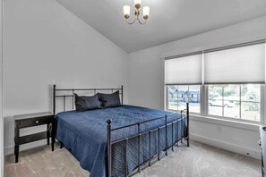 A bedroom with a bed, a nightstand, a window with blinds, and a chandelier. - Spacious Townhome with Fireplace (Ellicottville)