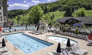 A pool area with lounge chairs, a water slide, and a view of a green landscape. - Spacious Townhome with Fireplace (Ellicottville)