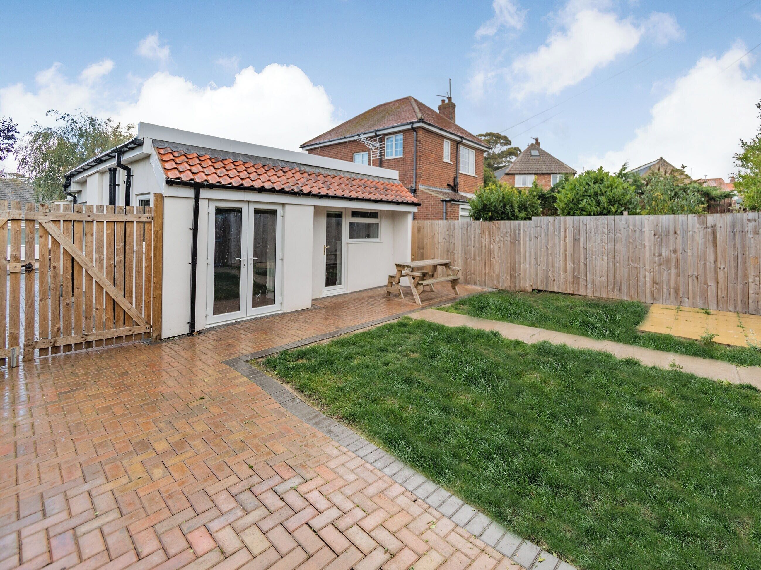 A backyard with a patio, a wooden fence, and a grassy lawn.