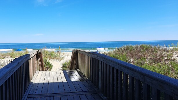 A wooden boardwalk leading to a beach with clear skies and ocean views.