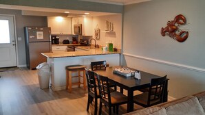 A compact kitchen with a refrigerator, microwave, and sink. There's a dining table with chairs and a small island with a sink. A lobster decoration is on the wall.