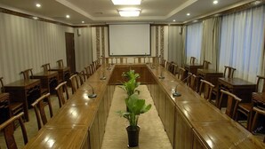 A conference room with a long wooden table, chairs, a projector screen, and a potted plant. - James Joyce Coffetel (Xi'an)