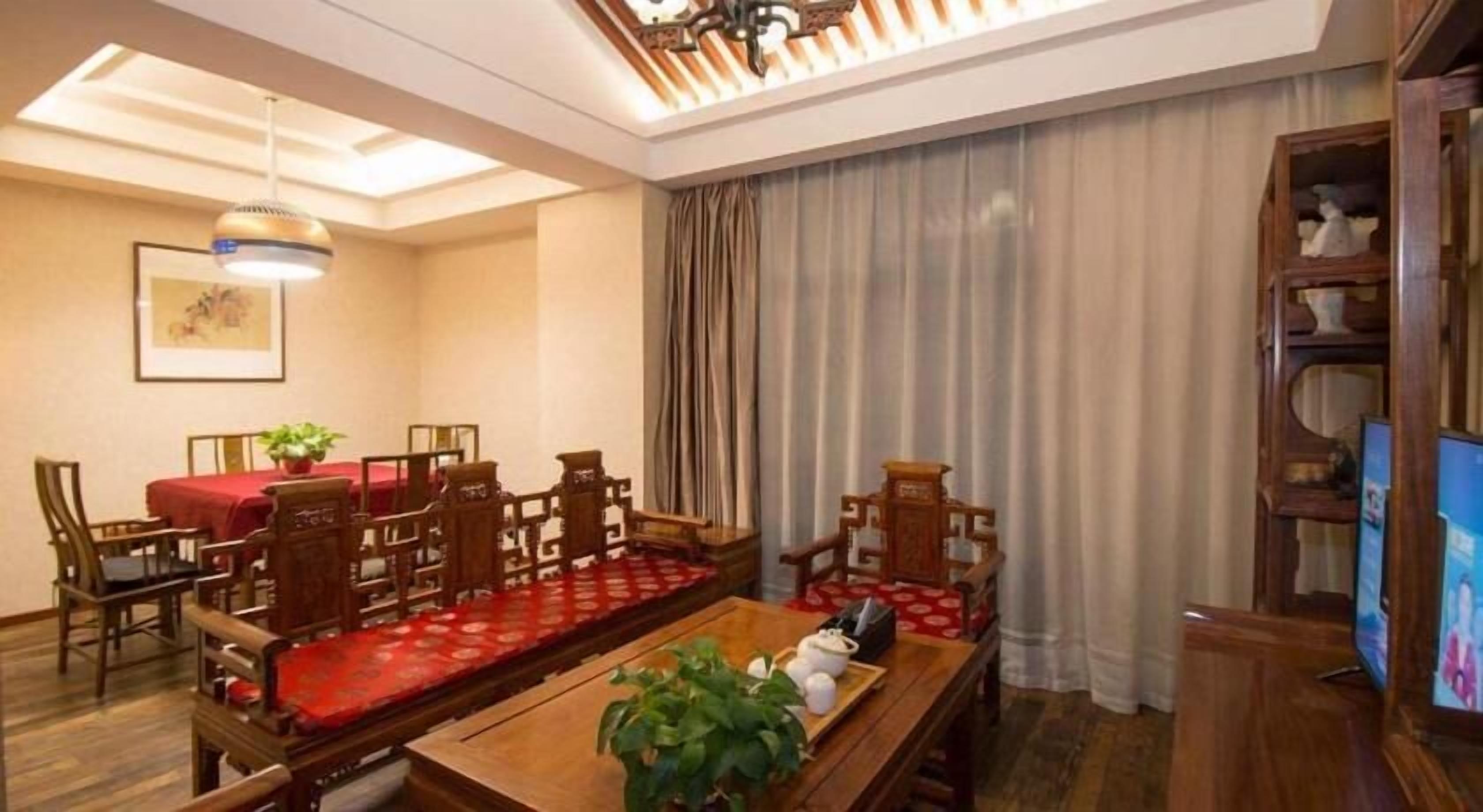 A dining area with a long wooden table, red tablecloth, and matching chairs. There is a television on the right and a plant on the table.