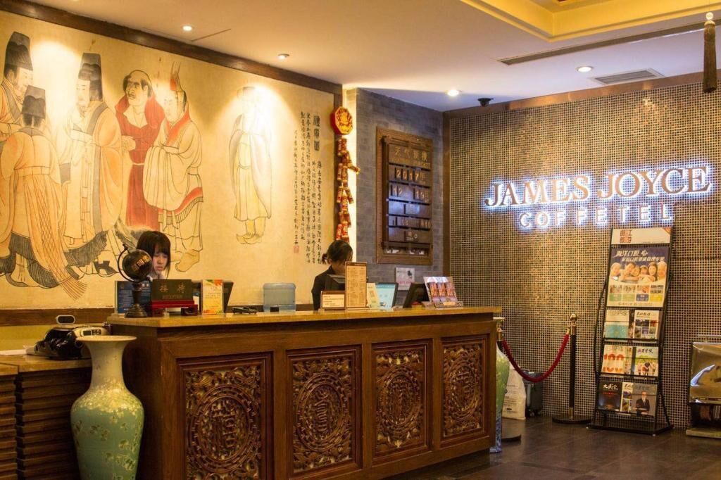 Un mostrador de recepción con un mural tradicional, un letrero de neón para el Hotel James Joyce Coffee y una barrera de cuerda roja.