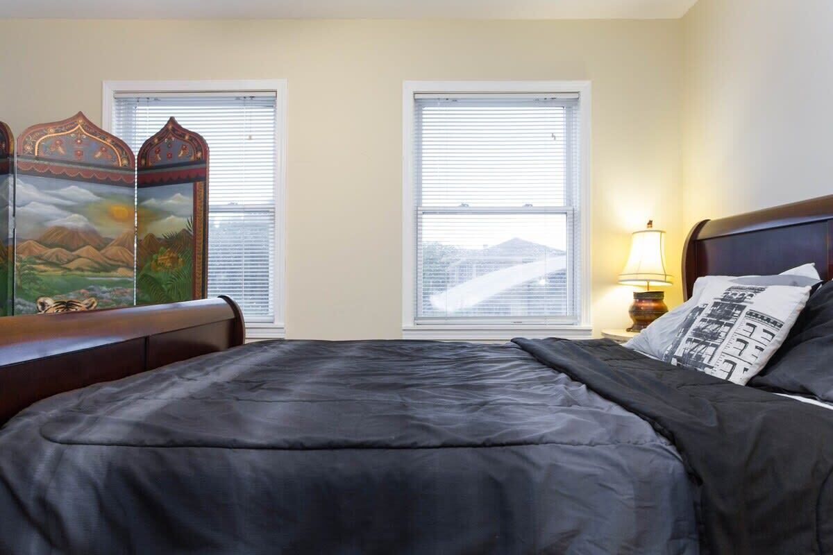 Una camera da letto con un letto, due finestre, un comodino con una lampada e un paravento decorativo.