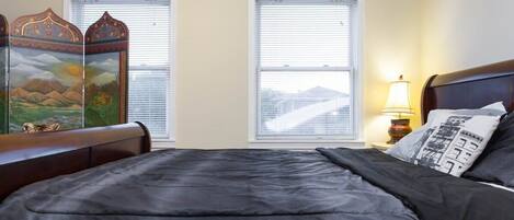 Una camera da letto con un letto, due finestre, un comodino con una lampada e un paravento decorativo.