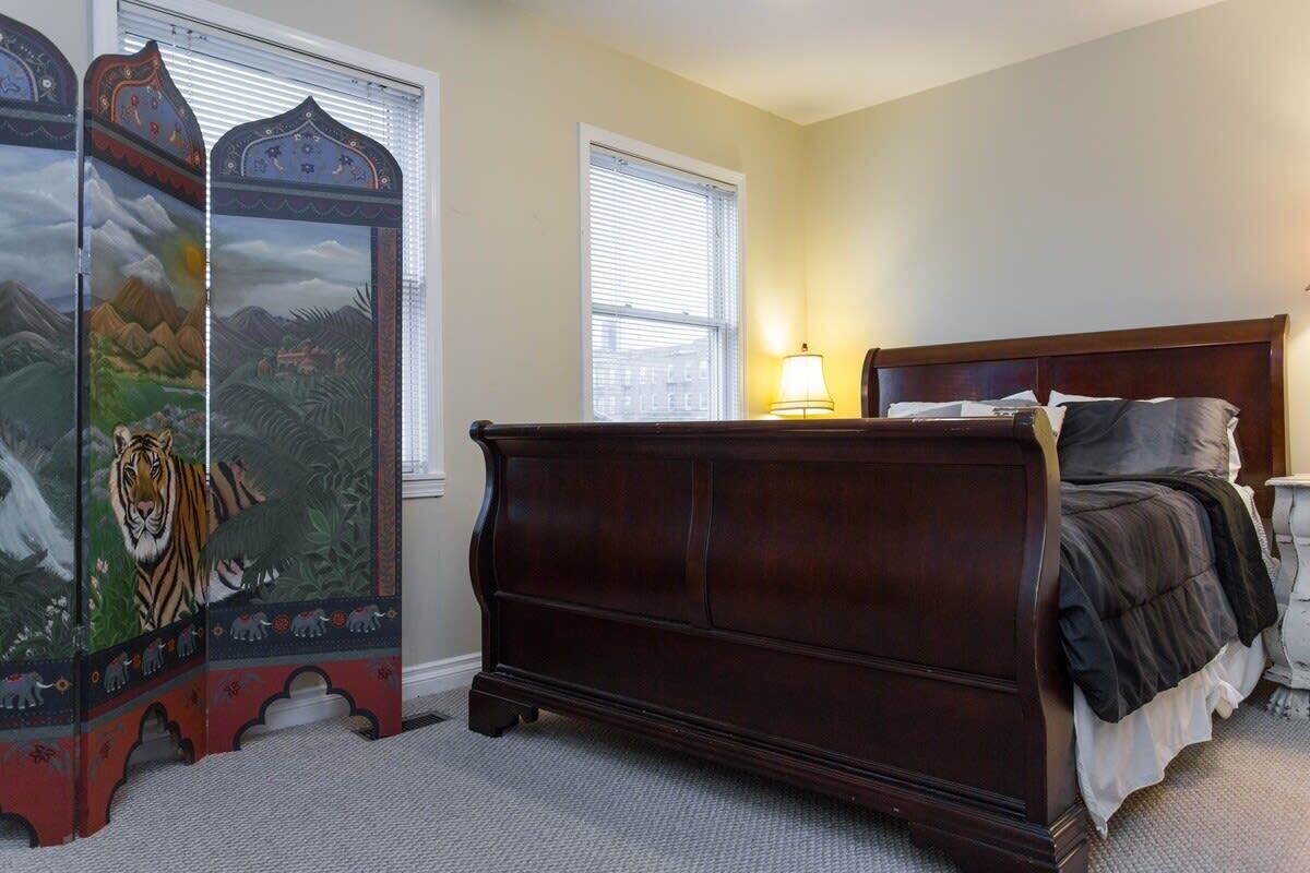 A bedroom with a wooden bed, a nightstand, a lamp, and a decorative screen with animal paintings.