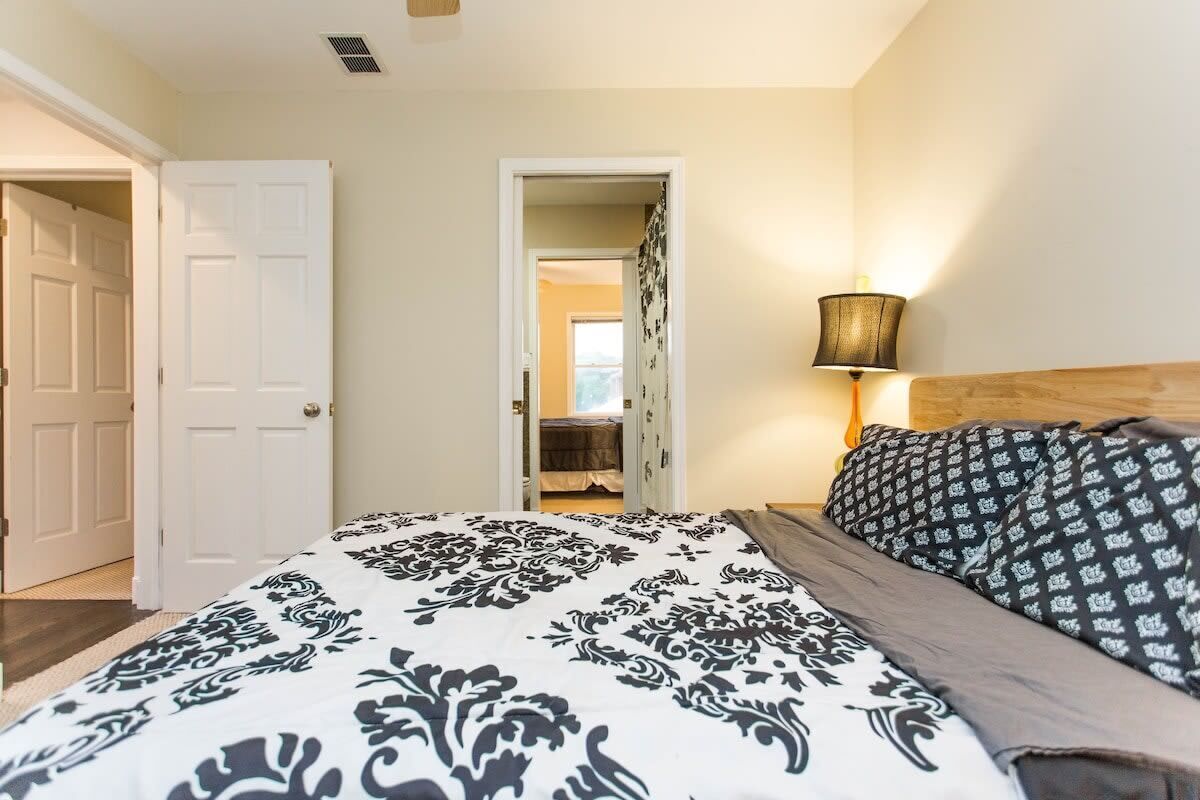 A bedroom with a bed, a nightstand, a lamp, and a door leading to another room.