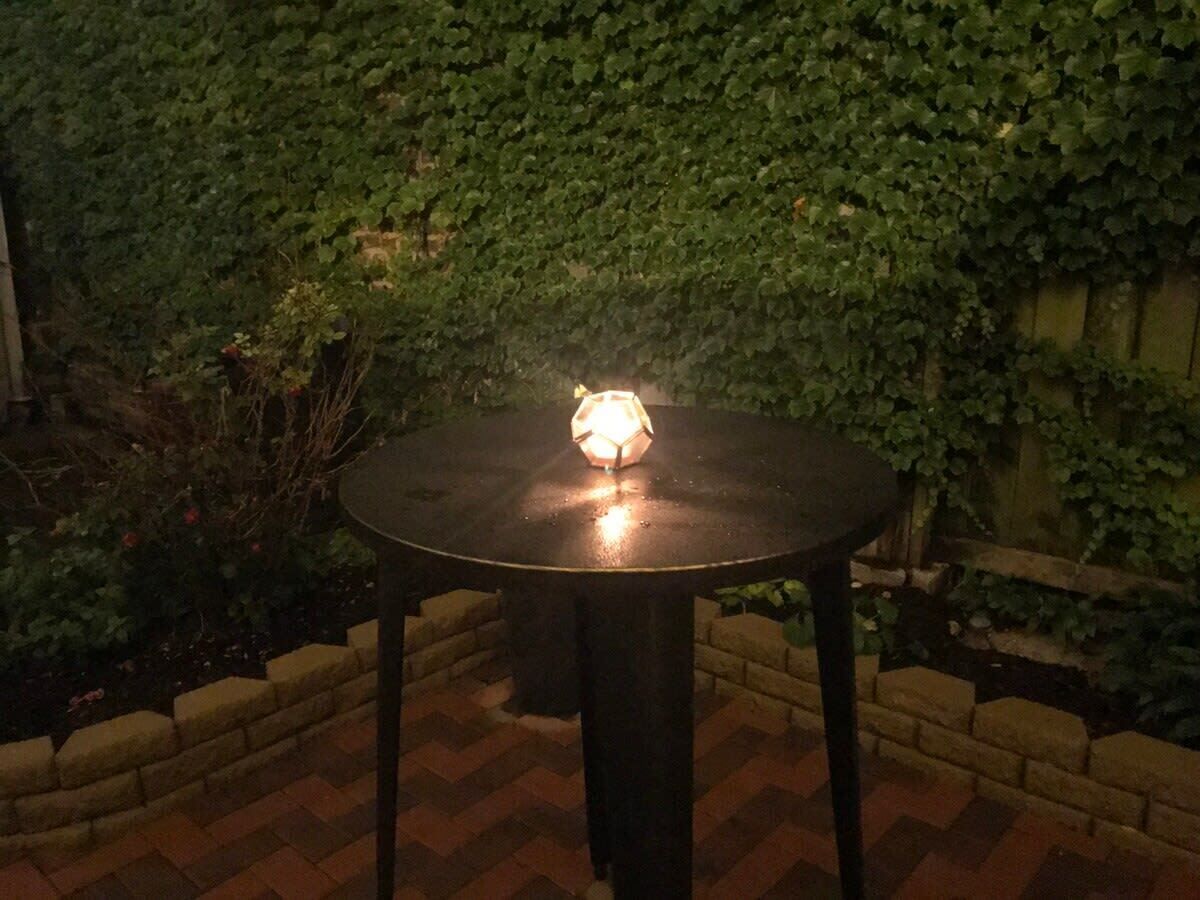 A round table with a light fixture in the center, surrounded by a brick wall and greenery.