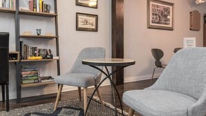 Una habitación acogedora con una estantería, dos sillones grises, una mesita redonda y cuadros en la pared.