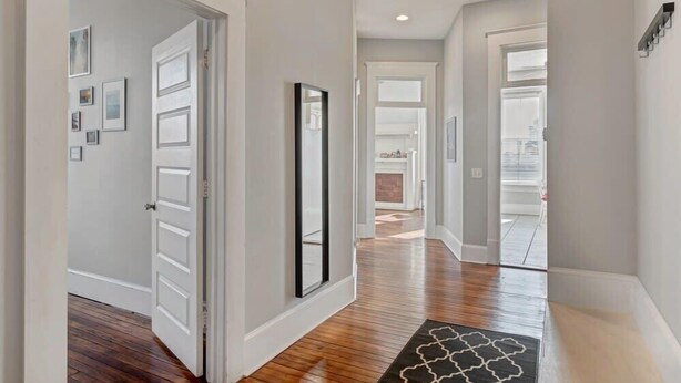 A hallway with wooden flooring, white walls, and a black and white patterned rug.