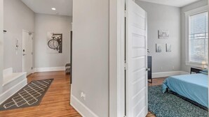 A bedroom with a bed, a window with blinds, a door, and a wall with a clock and artwork.