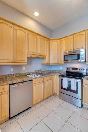 Una cocina con armarios de madera, lavavajillas de acero inoxidable, un lavabo, microondas y estufa.