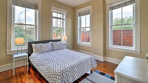 A bedroom with a bed, two bedside tables, a ceiling fan, and large windows with blinds. - Airy apartment in historic Springfield (Jacksonville)