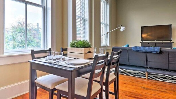 A dining area with a wooden table set for four, a sofa, and a television in the background. - Airy apartment in historic Springfield (Jacksonville)