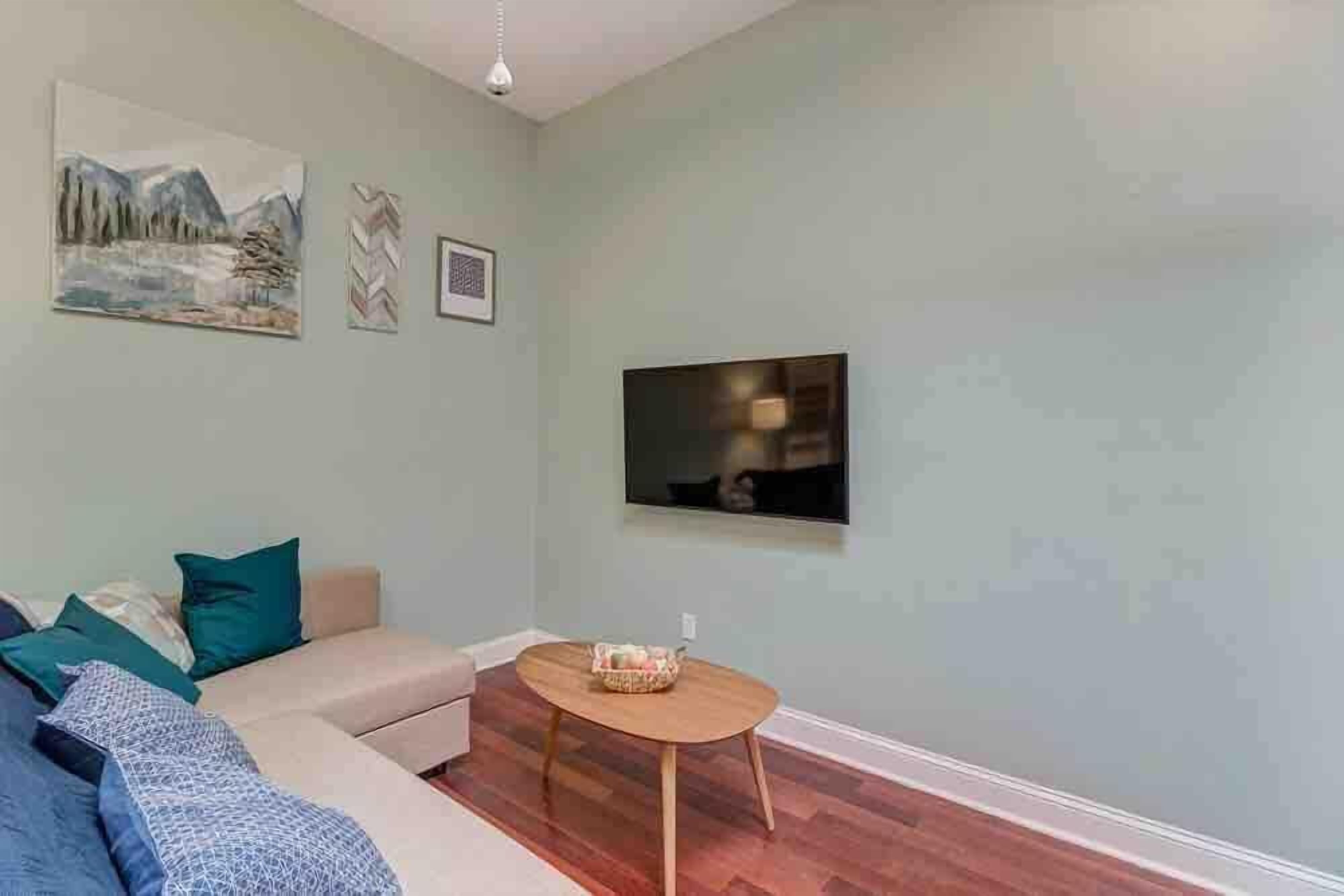 Una sala de estar con un sofá, una mesa redonda de madera y un televisor de pantalla plana montado en la pared.