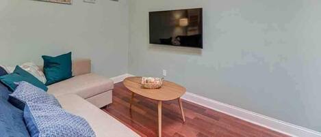 Una sala de estar con un sofá, una mesa redonda de madera y un televisor de pantalla plana montado en la pared.