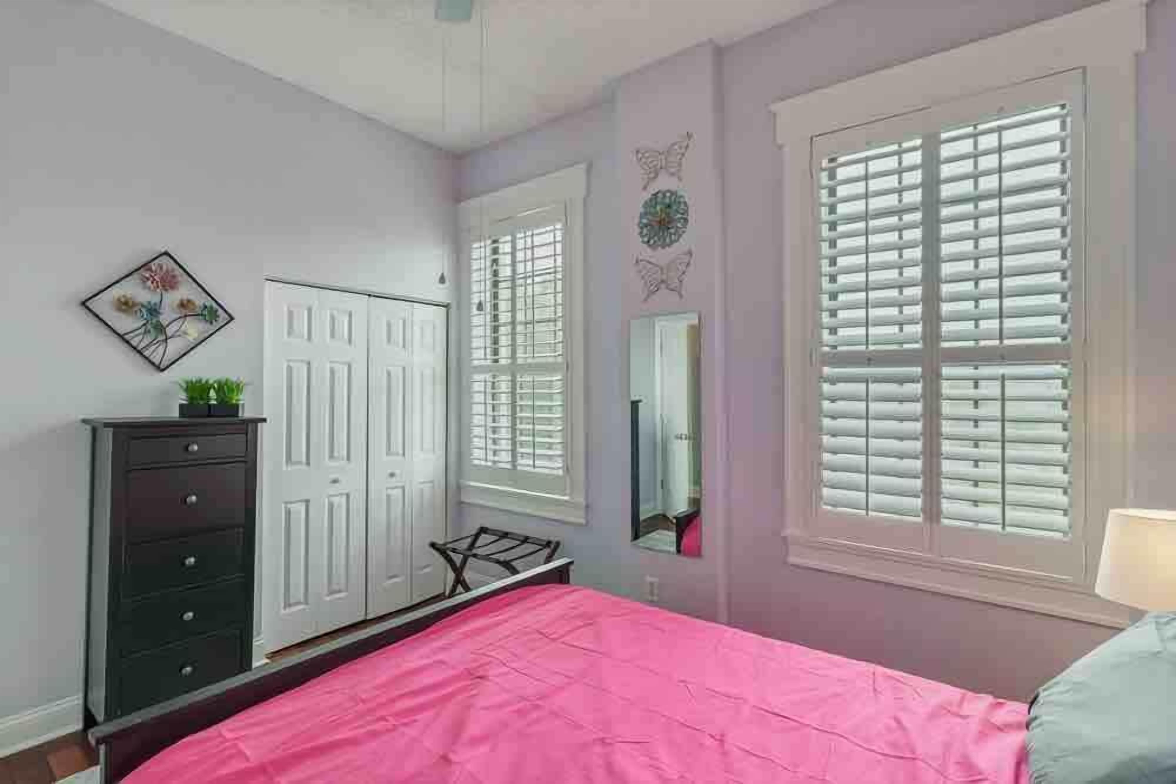 A bedroom with a bed, dresser, and two windows with blinds.