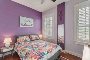 Un dormitorio con una cama, dos mesitas de noche, una ventana con persianas y una obra de arte colgada en la pared.