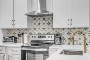 Una cocina con armarios blancos, una campana extractora de acero inoxidable, una estufa, un tostador y una cafetera.