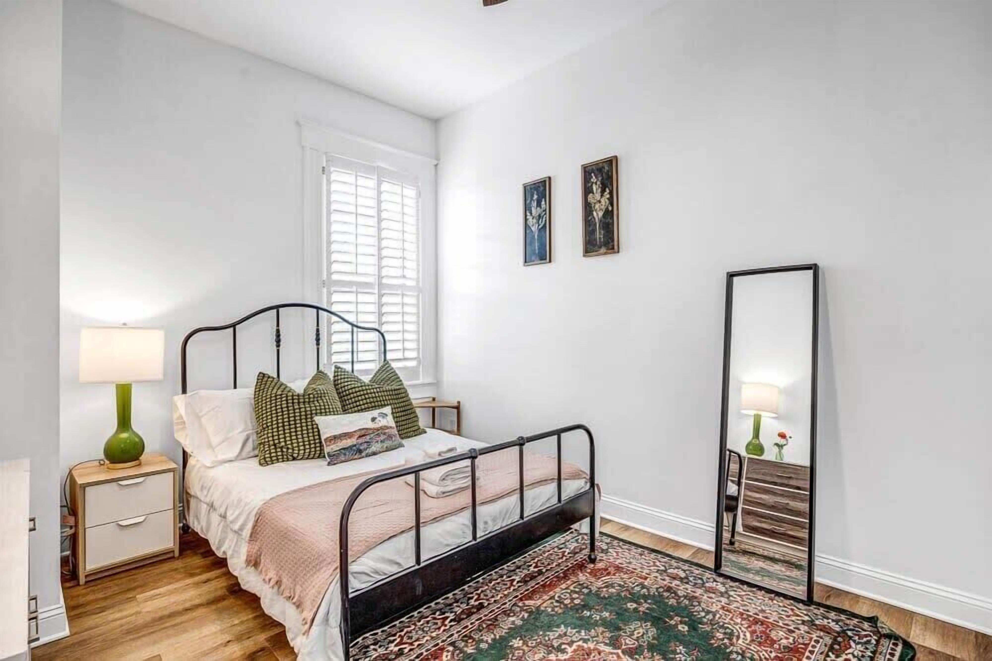 Een slaapkamer met een bed, nachtkastje, lamp en een grote spiegel.