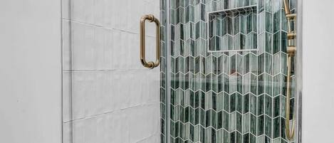 Eine gläserne Duschkabine mit Regendusche, kleinem Fenster und Handlauf.