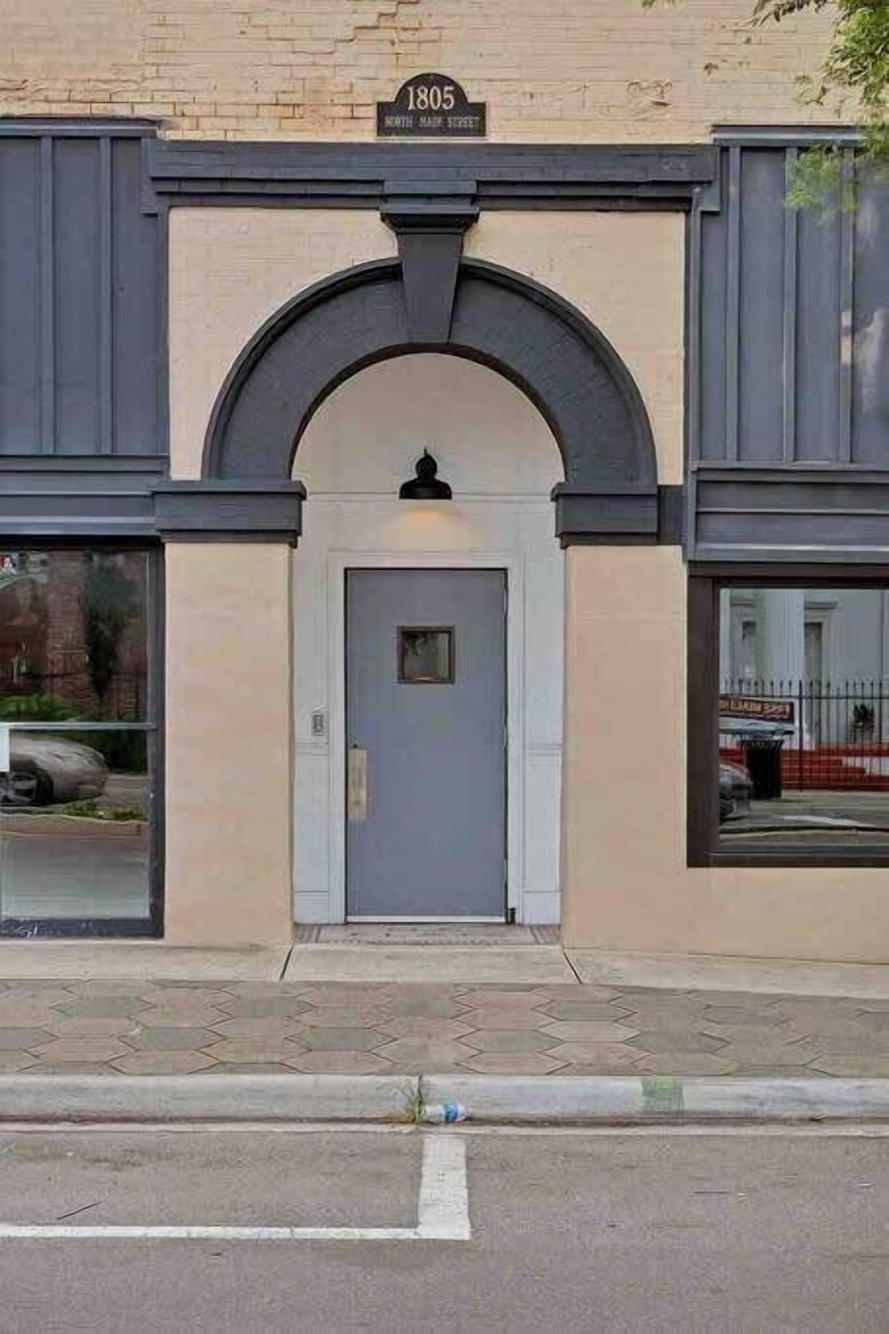 Un edificio con una entrada arqueada grande, una puerta y un cartel sobre la puerta.
