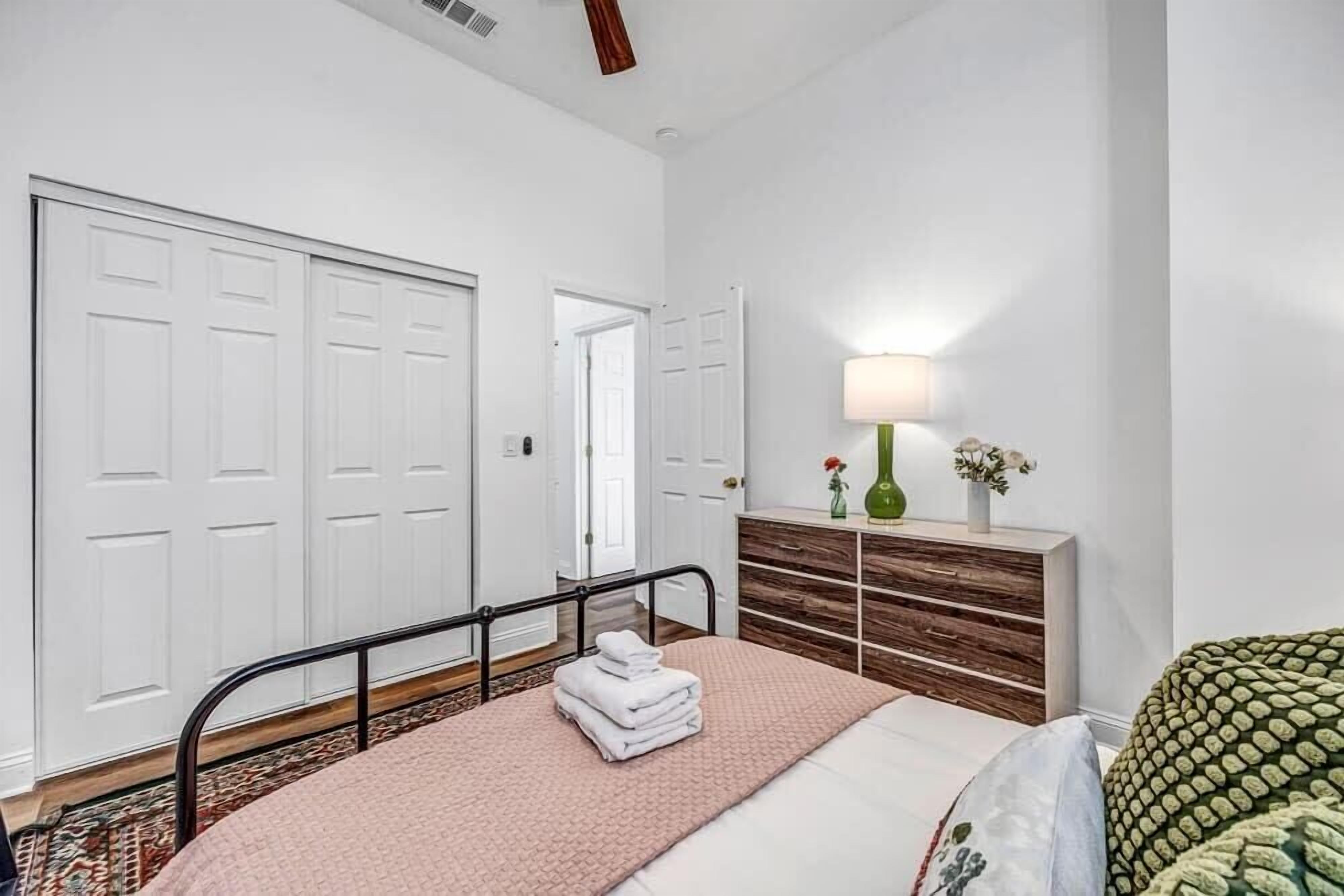 A bedroom with a bed, a bedside table with a lamp, a dresser, and a closet.