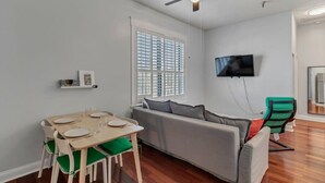 A compact living space with a dining area, a sofa, a television mounted on the wall, and a ceiling fan.