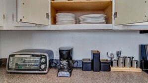 A kitchen with a toaster, coffee maker, and stacked plates on shelves.