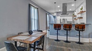 Een moderne keuken met een centraal eiland, barstoelen en een eethoek met een houten tafel en stoelen.